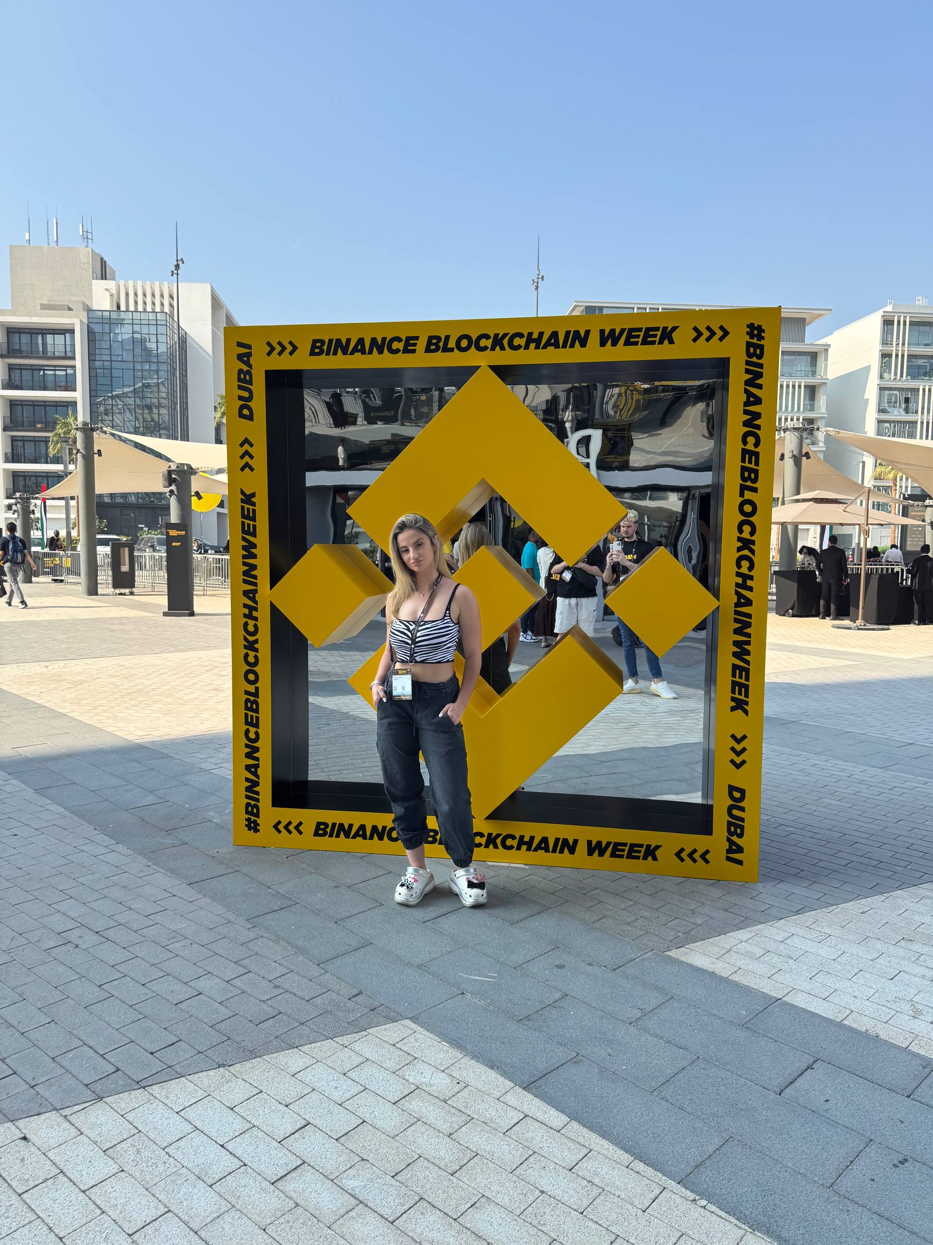 Jana standing in front of the Binance Blockchain Week Dubai logo frame